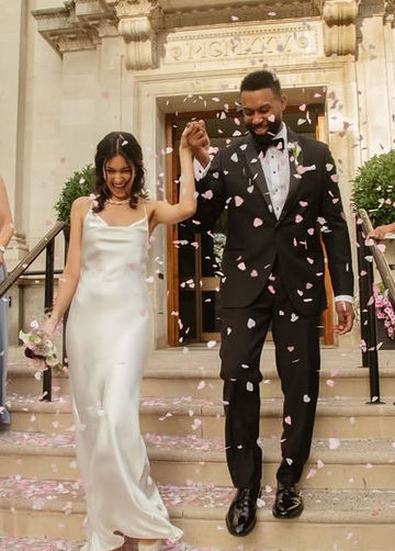 Laughing bride with soft glam makeup and a half-up hairstyle on the steps after her ceremony under petal confetti