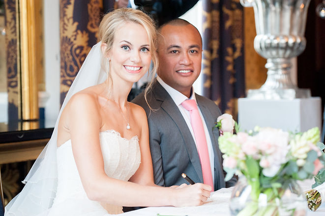 Bride with fresh wedding day makeup and a veil signing the register with her groom