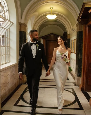 Smiling bride with natural glowing makeup and a half-up hairstyle walking hand in hand with her groom