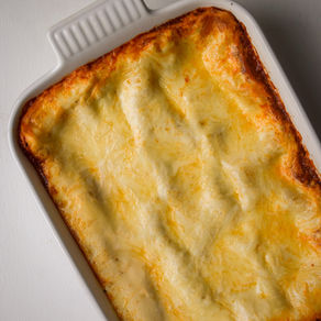 Overhead photo of golden baked béchamel lasagna with beef ragù in a white ceramic pan, showing bubbling edges and creamy layers.