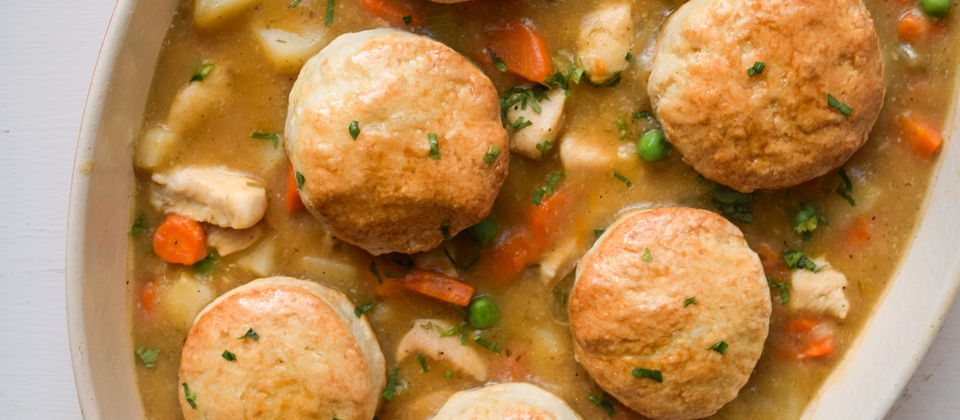 Creamy chicken pot pie filling with carrots, celery, peas, and diced potatoes, served in a skillet and topped with golden, flaky sourdough biscuits. Cozy homemade comfort food made with sourdough discard.