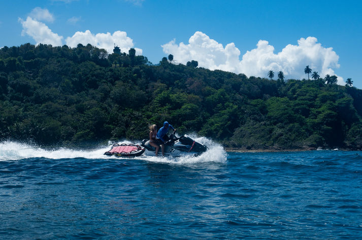 Two people ride jet ski near lush island