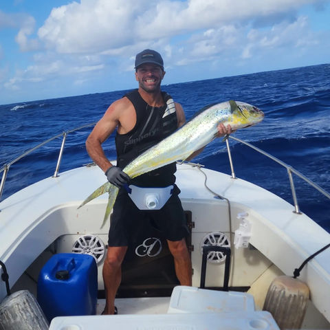 Smiling man holding large dorado fish on boat