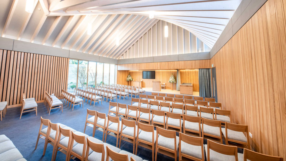 Photo of the interior of Guildford Crematorium Chapel from the back, showcasing the stunning vaulted roof, natural materials, and flexible seating arrangement. Visual tributes can be displayed on the front screen, and the chapel features underfloor heating for comfort.