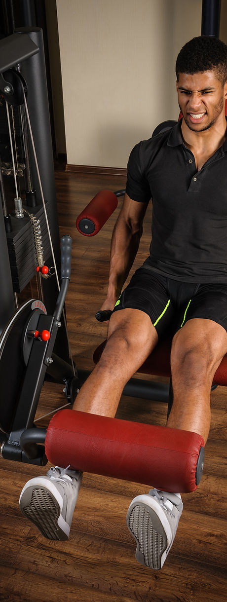 handsome young african descent mixed race man doing legs extensions workout in gym