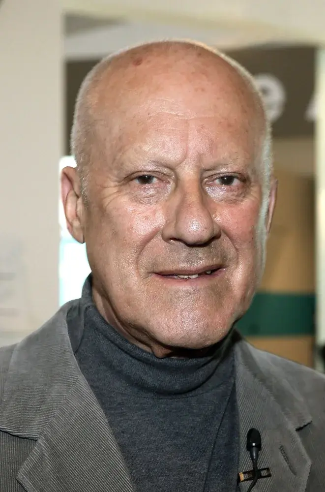 Norman Foster in a close-up portrait wearing a grey jacket and turtleneck, smiling slightly in an indoor setting.