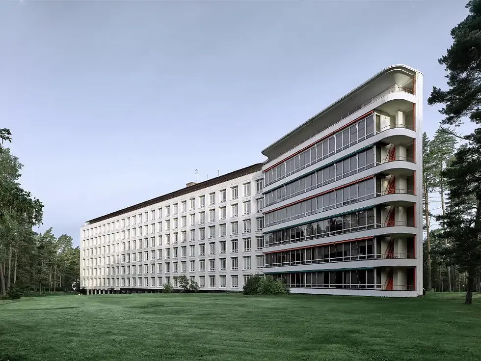 Paimio Sanatorium, a long white modernist hospital building surrounded by trees and green lawn, featuring balconies and ribbon windows.