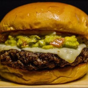 Close-up of a clean-label avocado veggie burger with creamy filling and toasted bun on a wooden board.