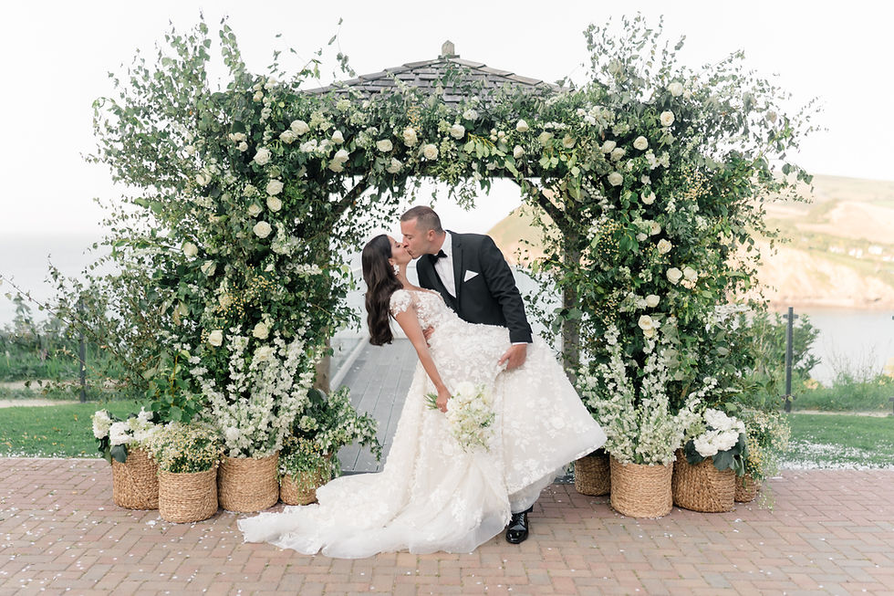 Bride and groom kissing in front of flower arch with white and green flowers captured by kent wedding photographer