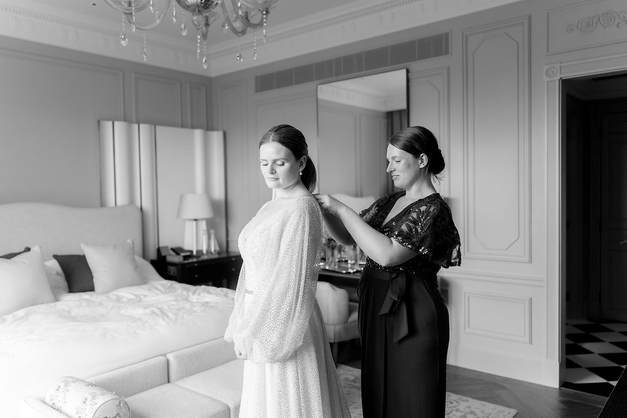 Bride having her dress done up by bridesmaid at savoy hotel wedding