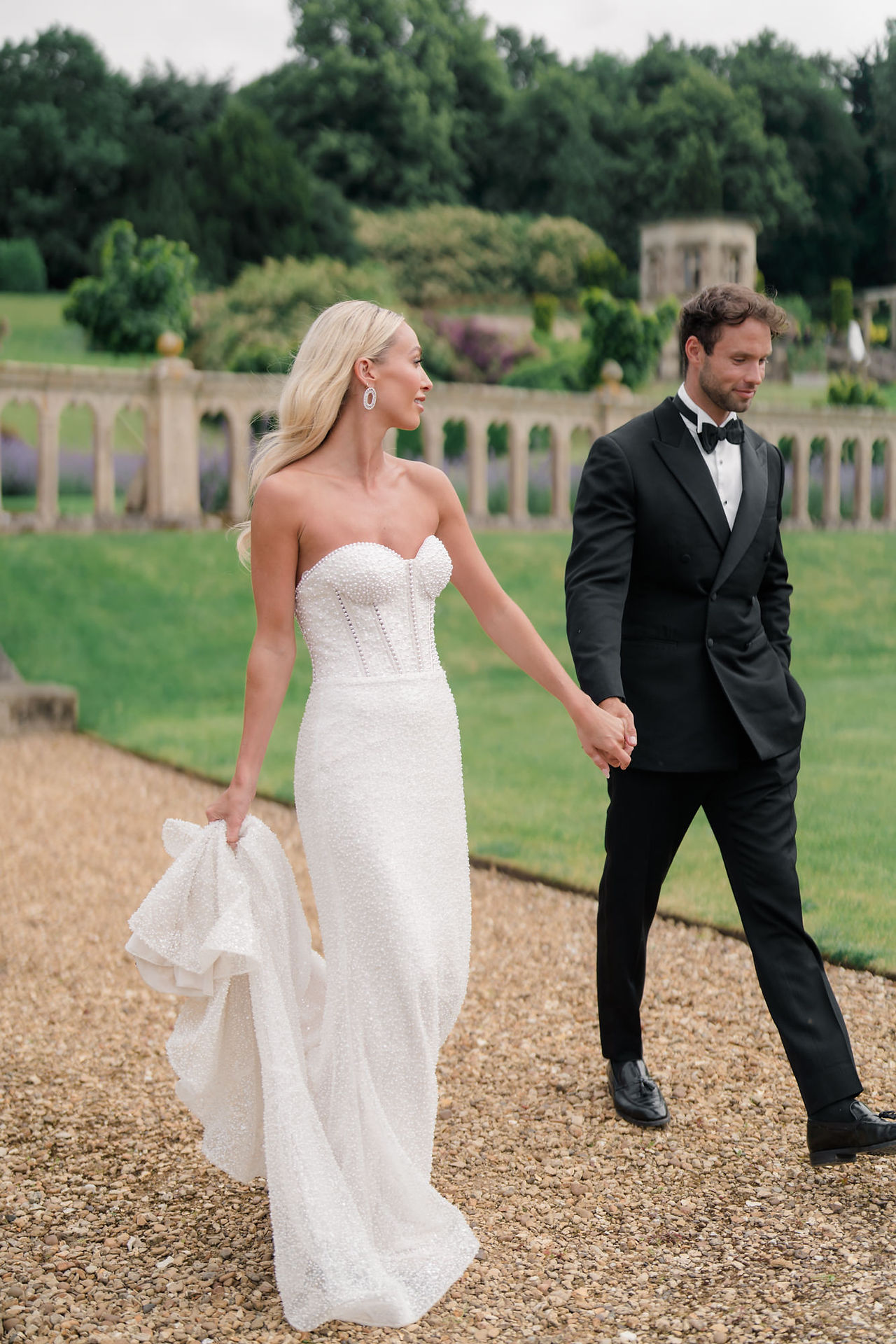 Bride and groom walking through gardens at Harlaxton Manor looking at one another