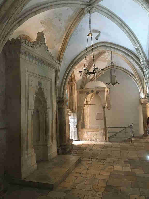Inside the Cenacle with a stone structure on the left and a staircase at the far end of the room