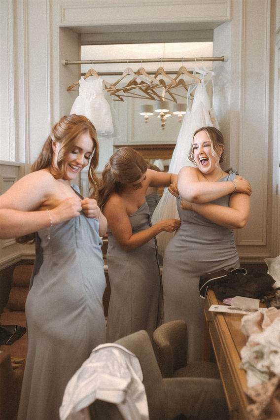 Bridesmaids getting ready together on a wedding morning, laughing and helping each other into dresses at Merewood Hotel, Lake District
