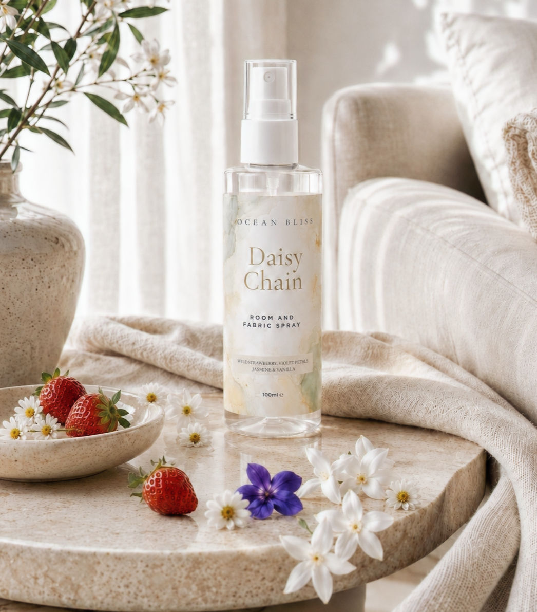 Daisy Chain room & fabric spray on a stone table next to a small bowl of fresh strawberries and white and purple flowers