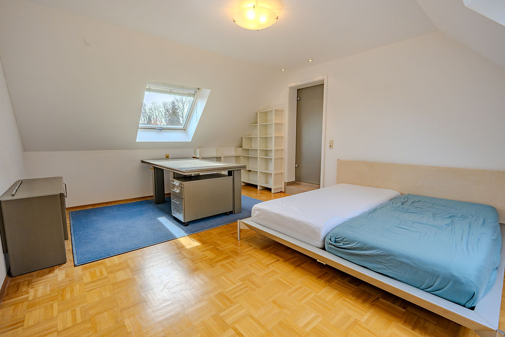 Helles Dachzimmer mit Bett, Schreibtisch und Holzparkett