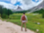 Hiker with backpack standing near Rifugio Palmieri, looking toward Becco di Mezzodì across alpine meadows in the Dolomites.