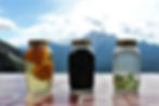 Three jars of homemade grappa infused with fruits and herbs at Rifugio Scotter, with Mount Pelmo and the Dolomites in the background.