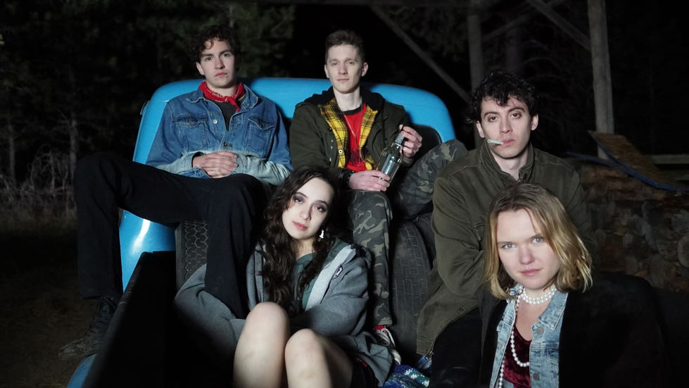 Band members, three guys and two girls, all sitting in the bed of an old 1940s light blue truck.