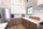 Modern kitchen with white and wood cabinets, stainless steel fridge, marble countertops. Cutting boards and coffee maker are on the counter.