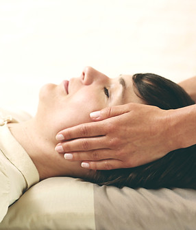 Frau l iegt entspannt auf Massageliege während heilende Hände an ihrem Kopf liegen