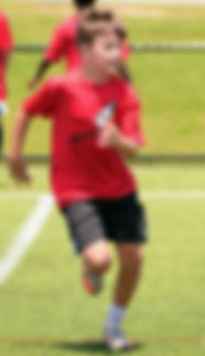 A young boy wearing a red shirt and black shorts playing soccer at a one of Coach Salsa's soccer clinics.