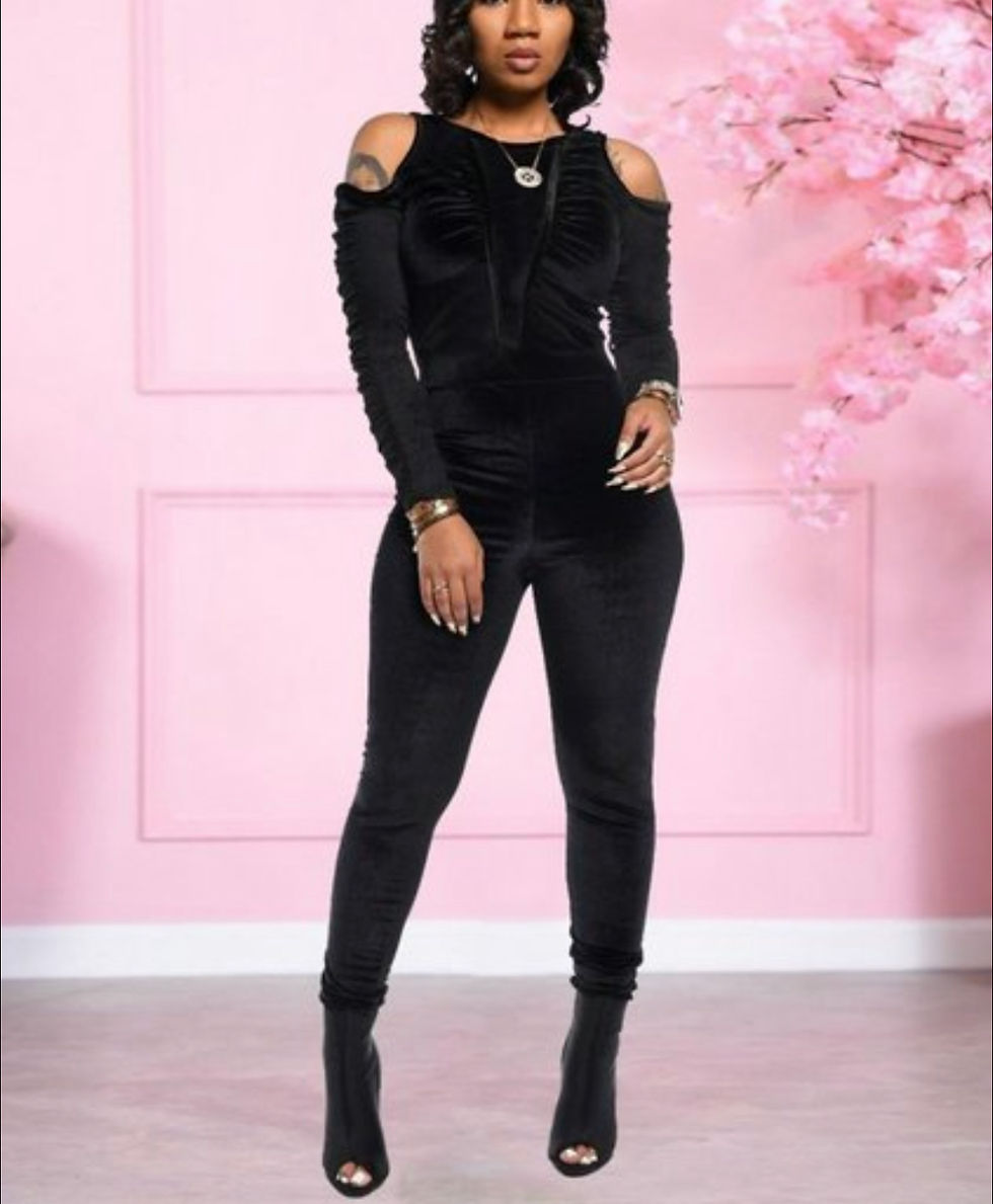 Thumbnail: Woman in a black Velvet Ruched Skinny Jumpsuit posing in front of pink flowers.