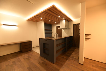 木目の下がり天井と間接照明に照らされた対面キッチン。左手に造作カウンターがある