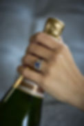 Hand holding champagne bottle wearing sapphire and diamond ring