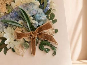 Pressed blue hydrangea bouquet with a velvet ribbon bow, framed as a gift on a wooden surface