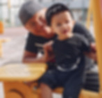 Father and sun joyfully play together on a colorful playground filled with swings and slides.