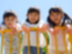 Three young girls smiling and playing while standing on a yellow tower fence, surrounded by colorful playground equipmen