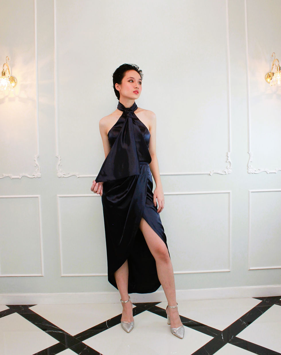 A short haired lady wearing a JACQ midnight blue halter neck with skirt draping cocktail dress.