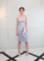 A short haired lady wearing a light gray JACQ coctail crop top and draped skirt set.