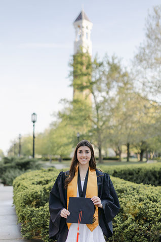 graduate standing in front of the bell tower holding a hat
