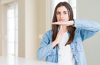 Femme en chemise en jean faisant un signe de pause avec les mains dans un intérieur lumineux.