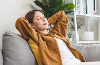 Femme détendue assise sur un canapé, les mains derrière la tête, profitant d’un moment de relaxation et de bien-être.