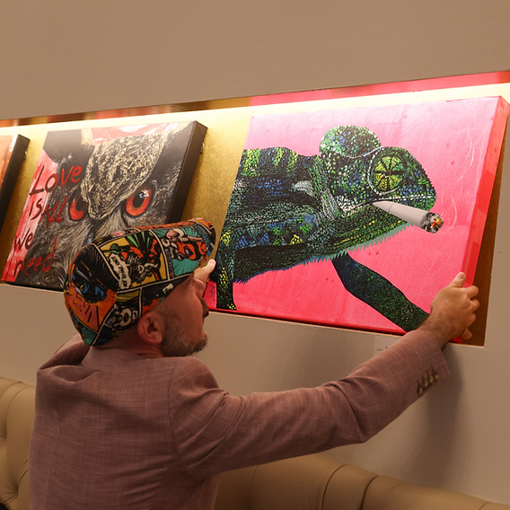 Wiener Künstler Markus Buchsbaum in seiner aktuellen Ausstellung im Hotel Rathaus Wien und Design im 8. Wiener Gemeindebezirk wie er gerade ein Gemälde mit Chamäleon positioniert.