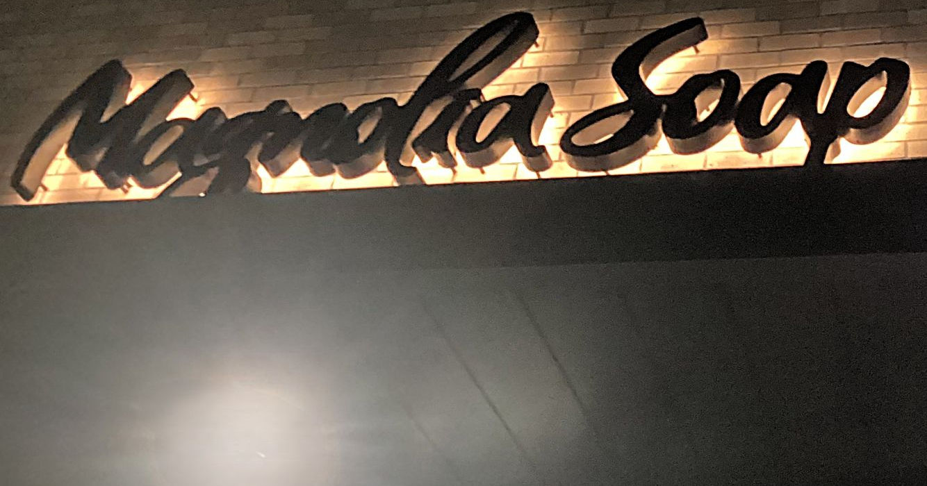 Closeup night view of a custom white LED halo-lit black channel letter wall sign installed on a brick building by Mello Signs