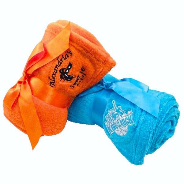 Promotional blue and orange blankets with embroidered company names and logos, rolled and tied with a ribbon for giveaways.