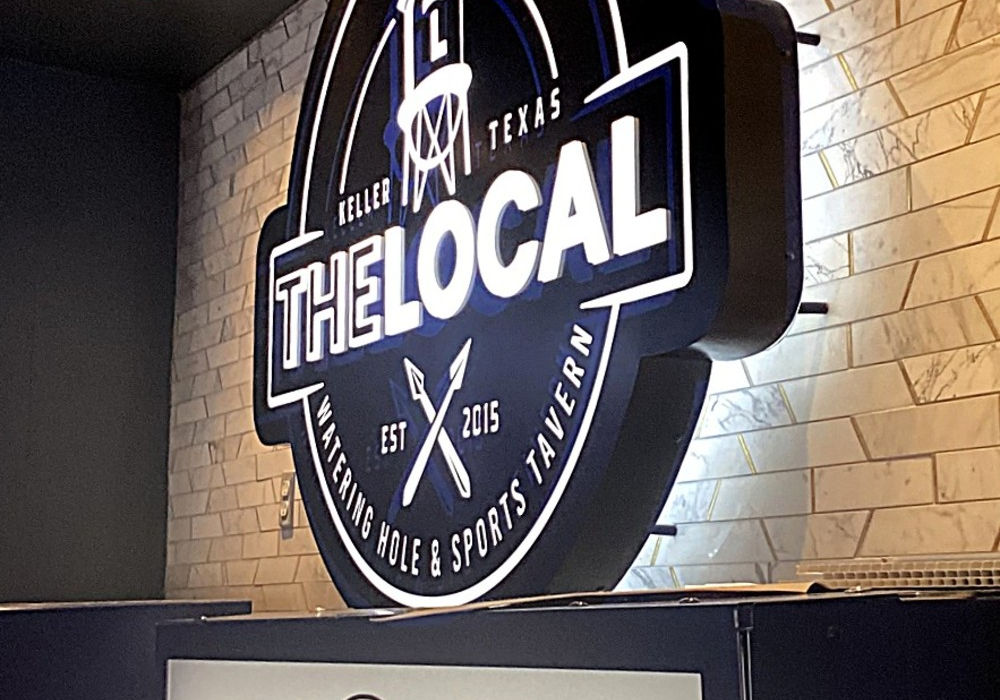 Custom routed black & white push-thru cabinet wall sign with LED halo lighting installed on a tavern wall by Mello Signs DFW.