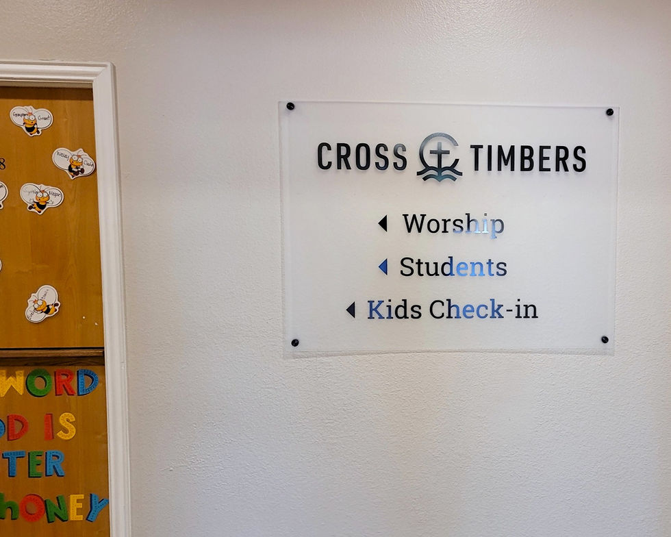 Interior hallway wayfinding sign made on clear acrylic with black vinyl, installed with standoffs, on a tan wall by a door.