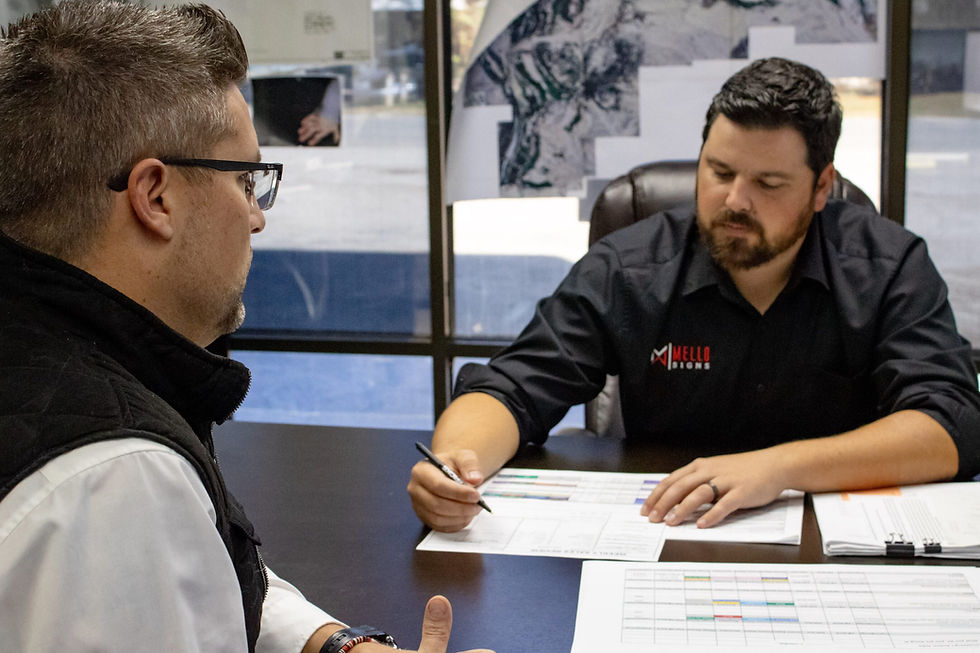 Joe Mello sitting at a desk across from another man working on a timeline for a sign project and sign permitting.