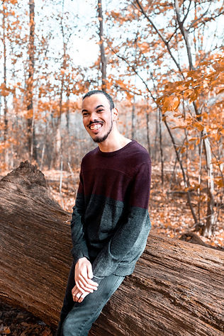 Photo of David Wadley sitting on a log in an autumnal forest. Credit @matthewsaylor https://linktr.ee/matthewsaylor