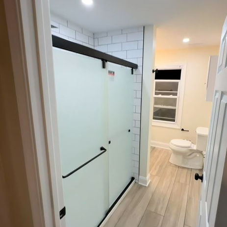 Bathroom renovation in Mansfield NJ featuring a frosted sliding glass shower, subway tile walls, and wood-look tile flooring.