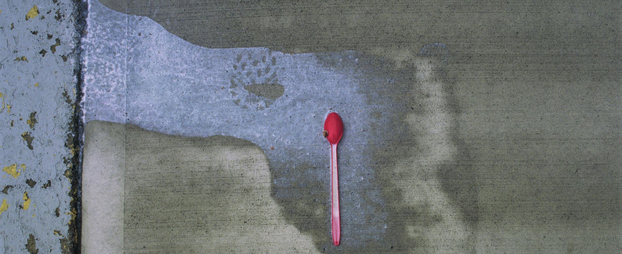 35mm photo of dropped ice cream with a red plastic spoon. the melted ice cream ran off the side walk. 