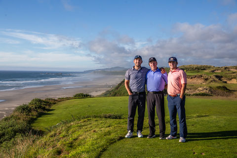 Three golfers in navy blue and sky-blue attire, high-fiving after playing on the green at Sheep Ranch, the newest course at Bandon Dunes, captured with a Canon DSLR and a wide-angle lens. The image showcases their joyful interaction against a backdrop of greenery. Photo by Angela Cardas of Bandon Golf Photography