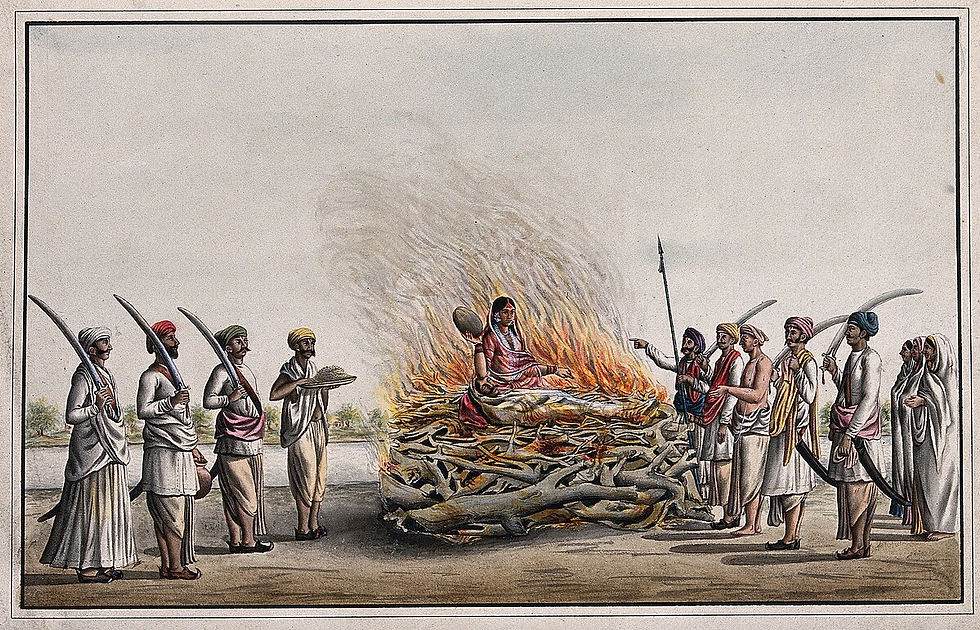 A woman in a red sari sits on a funeral pyre surrounded by people, some holding swords. Flames rise, creating an intense scene.