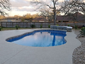 Freeform fiberglass pool design with stone wall feature and light concrete deck