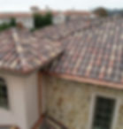 The corner of a homes roof showcasing a light red and dark red tile roof pattern.