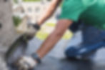 Roofer applying roofing membrane near a chimney base.